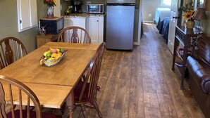 A kitchen with wooden cabinets, a refrigerator, a dining table with chairs, and a wooden floor. - Attractive Country Get-a (Abbeville)