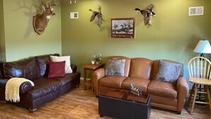 A living room with a brown leather sofa, a wooden coffee table, and a ceiling fan. - Attractive Country Get-a (Abbeville)