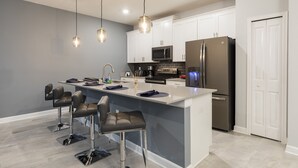 A modern kitchen with white cabinets, stainless steel appliances, and a central island with bar stools. - Champions Gate-8919ltsdjgilthp (Davenport)