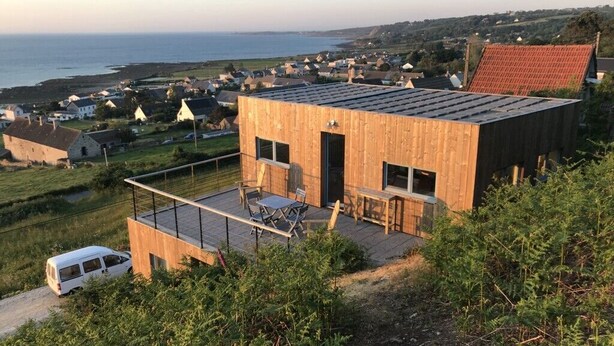A modern house with a flat roof, a balcony, and a view of the sea.