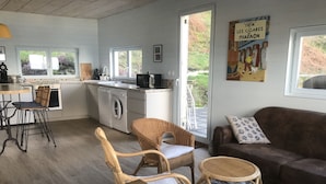 A cozy living area with wicker furniture, a sofa, and a coffee table. There is a kitchen with a washing machine and a dining area with chairs.