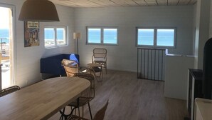 A spacious room with a wooden ceiling, a large table, wicker chairs, and a view of the sea through windows.