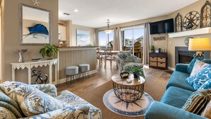 A spacious living room with a large sofa, a coffee table, and a dining area with a view of the outside. - Dock Holiday: Canalfront condo, Water Views, Fisherman's dream with Boat Dock (Manteo)