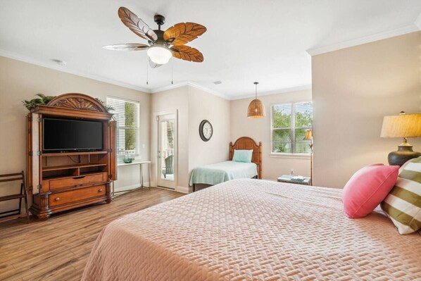 A bedroom with a bed, a wooden TV stand, a ceiling fan, and a window.