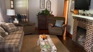 Ein Wohnzimmer mit Kamin, einem darüber montierten Fernseher und einem karierten Sofa.