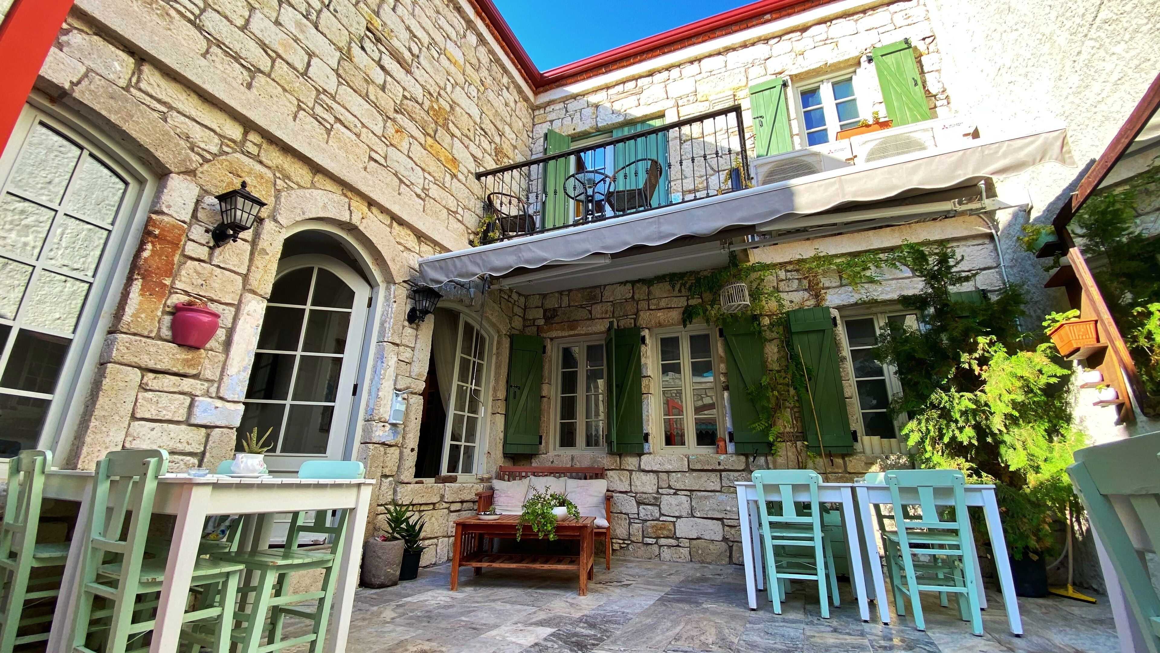 Ein Steinhaus mit Balkon, Außenbestuhlung und Topfpflanzen.
