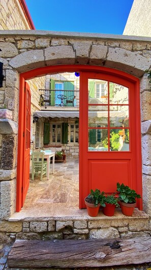 A stone archway leading to a courtyard with a red door, potted plants, and a view of a green-roofed building in the background. - Oberj d'Azur Alacati (Cesme)