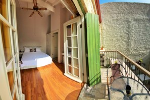 Ein Schlafzimmer mit Holzboden, einem Bett und einer grünen Tür, die auf einen Balkon mit Bergblick führt.