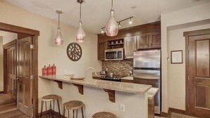 A kitchen with a central island, wooden cabinets, a stainless steel refrigerator, and pendant lighting. - 2 Bedroom Blackbear Lodge Condo in River Run Village (Keystone)