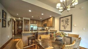 A modern kitchen with wooden cabinets, a central island, and a dining area with wicker chairs. - Luxury 1 Bedroom Ski in, Ski Out Mountain Vacation Rental Just Steps from the Snowflake Ski Lift in Breckenridge (Breckenridge)