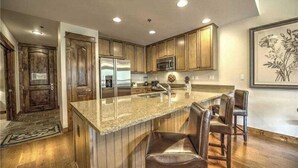 A modern kitchen with wooden cabinets, a stainless steel refrigerator, and a granite countertop. - Luxury 1 Bedroom Ski in, Ski Out Mountain Vacation Rental Just Steps from the Snowflake Ski Lift in Breckenridge (Breckenridge)