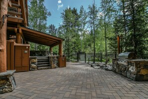 A covered outdoor area with a stone barbecue and a wooden grill, surrounded by a stone wall and a metal fence.