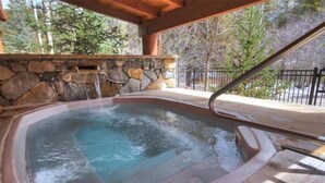 Un bain à remous avec un mur en pierre en arrière-plan, une terrasse en bois et une rambarde en métal.