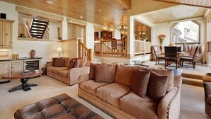 Un vaste salon doté d’un haut plafond, de poutres apparentes, d’un ensemble de canapés, d’un coin repas avec des chaises et d’un escalier menant à un autre niveau.