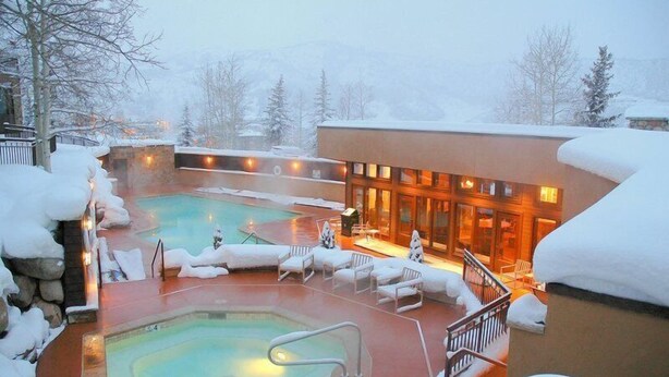 Un espace extérieur avec une piscine recouverte de neige, des chaises longues et un bâtiment doté de grandes fenêtres.