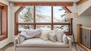 A cozy room with a large window, a sofa, and a floor lamp. - Snowmass Woodrun V 2 Bedroom Ski in, Ski out Mountain Residence in the Heart of Snowmass Village (Snowmass Village)