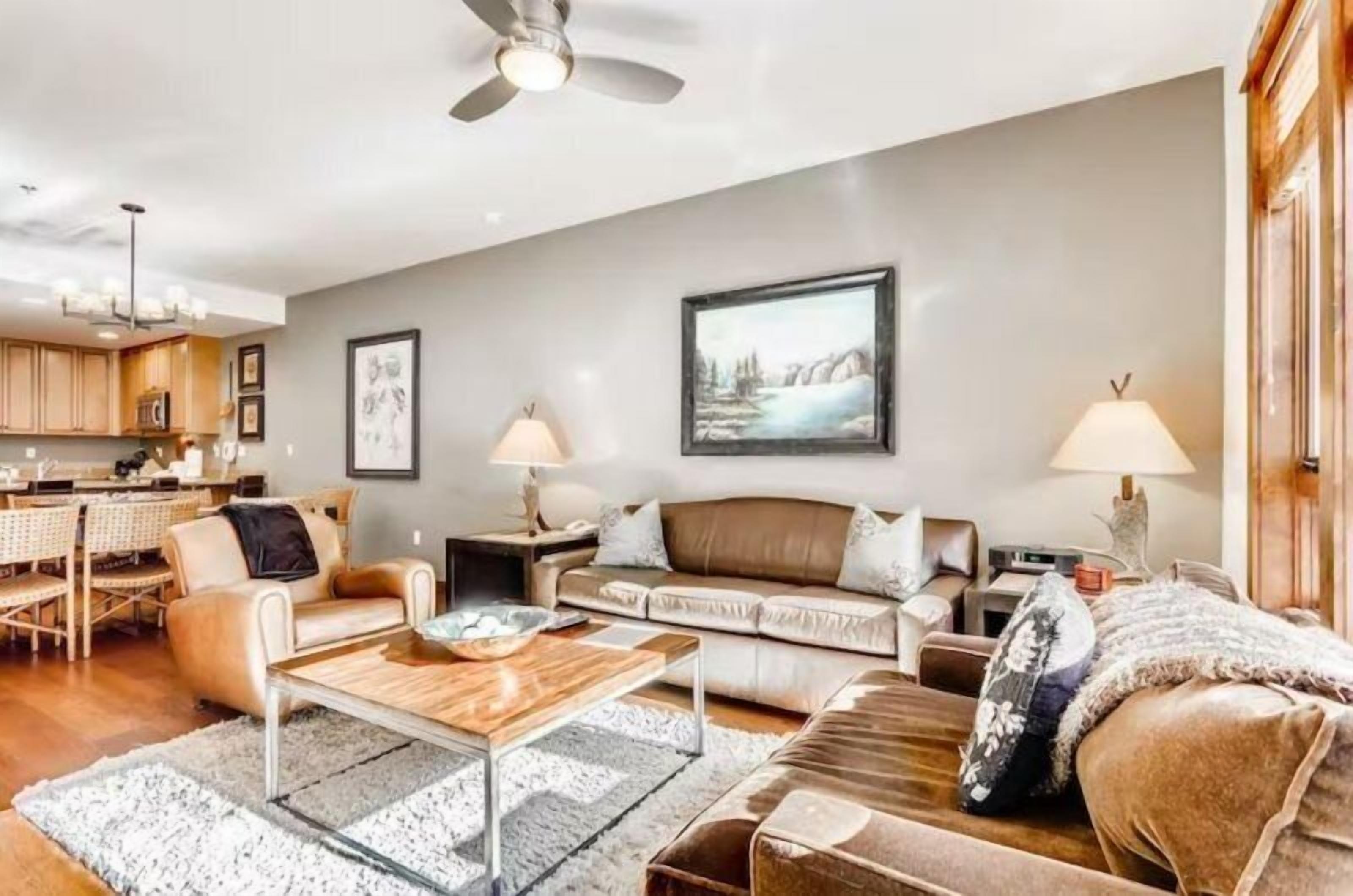 A spacious living room with a sofa, coffee table, and two lamps. There is a dining area with a table and chairs in the background.