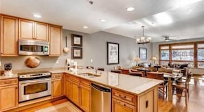 Kitchen features a large island with a sink, microwave, oven, and dishwasher, adjacent to a dining area with a sofa and table.