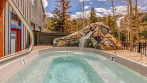 A hot tub with a waterfall feature, surrounded by a stone wall and a metal railing.