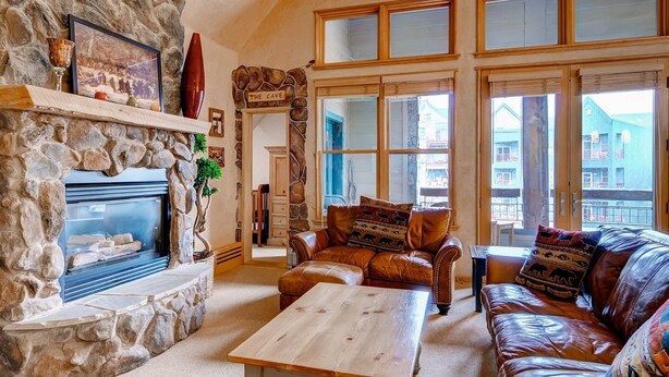 A cozy living room with a stone fireplace, leather sofas, and large windows offering a view of the outside.