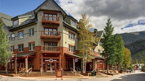 A multi-story hotel with a prominent entrance, outdoor seating area, and a mountain backdrop.
