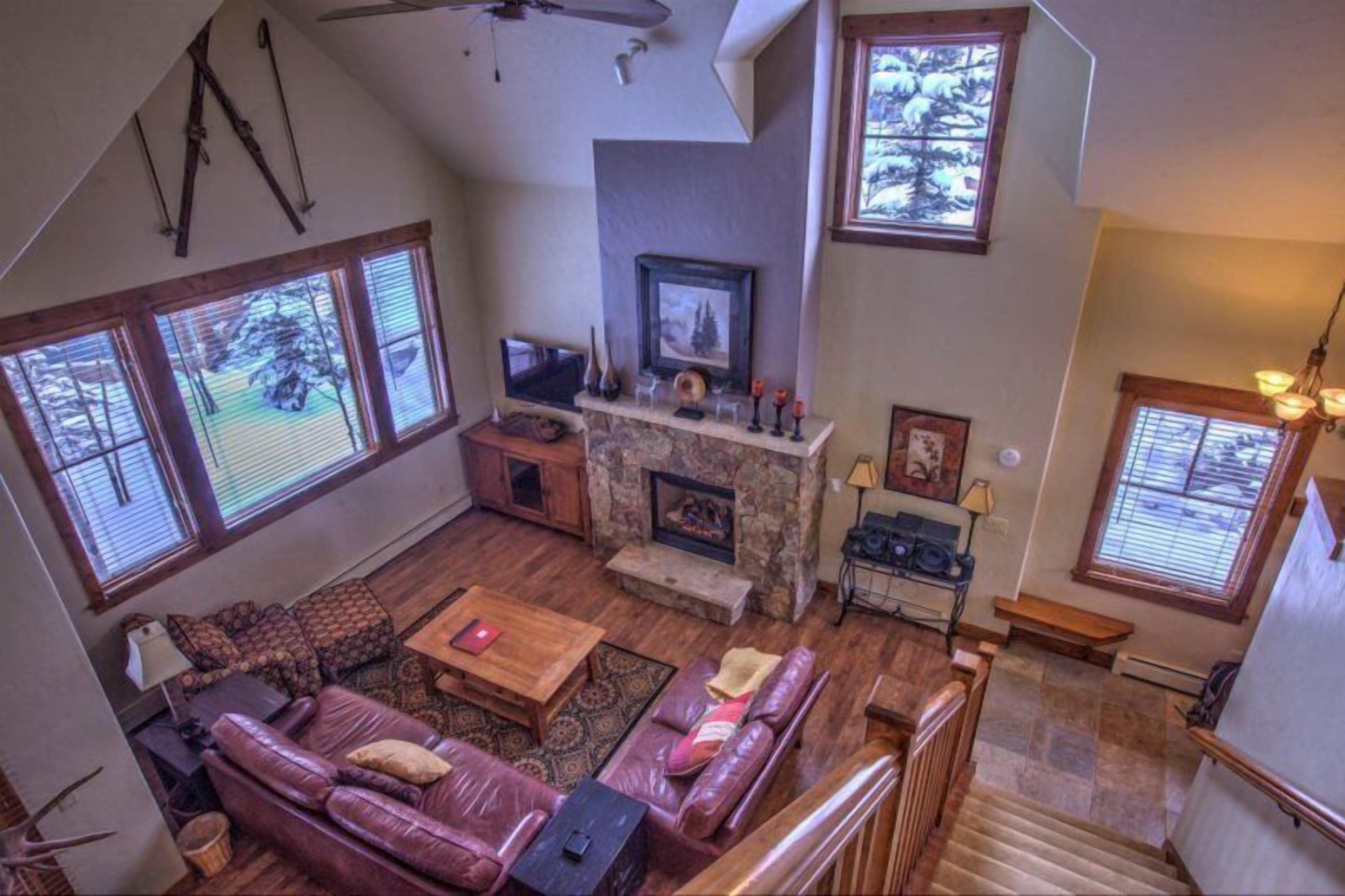 A spacious living room with a stone fireplace, leather sofas, and large windows.