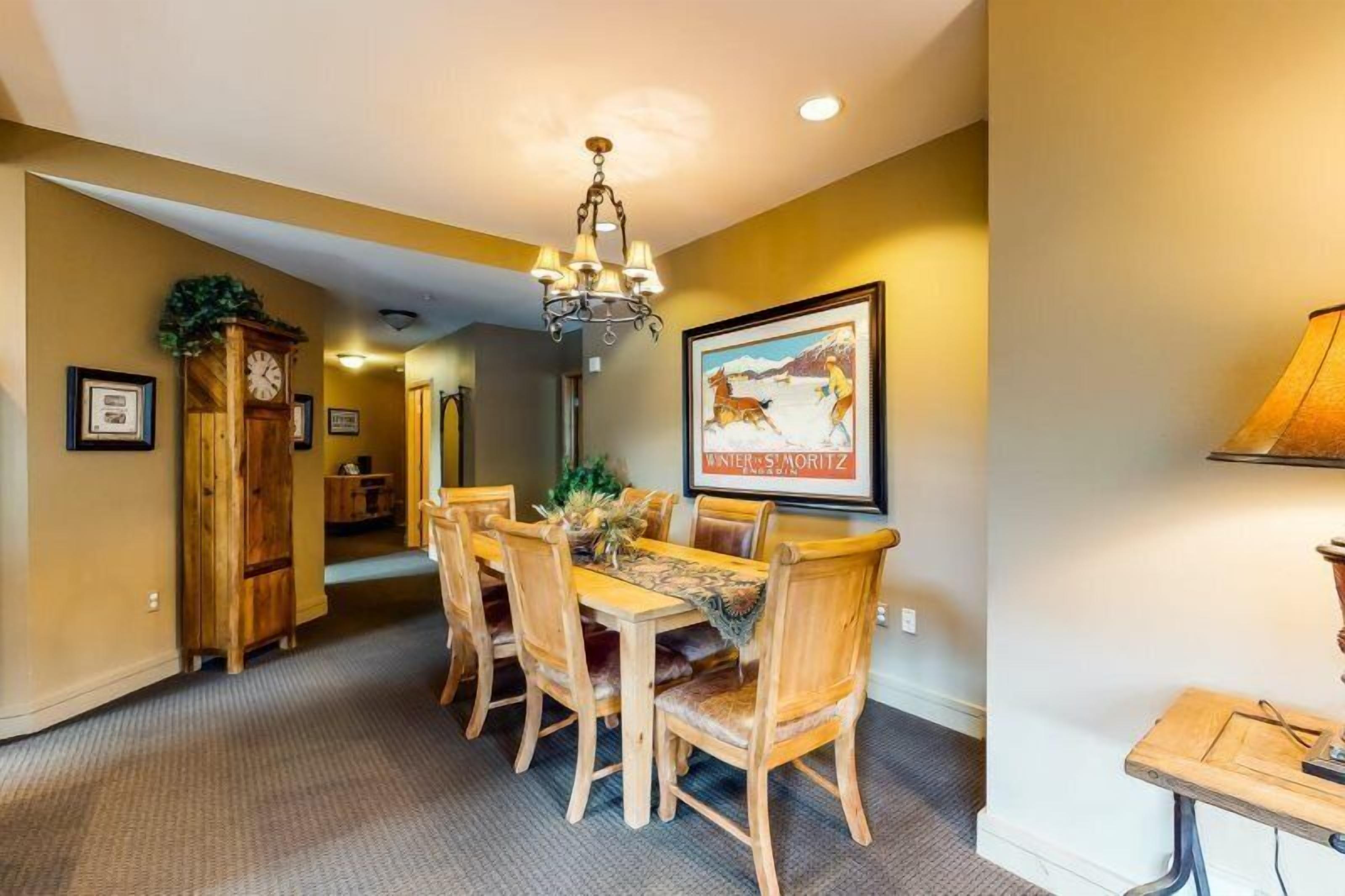 A dining area with a wooden table and chairs, a chandelier, and a framed picture on the wall.
