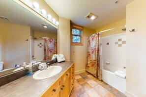 Ein Badezimmer mit großem Spiegel, Waschbecken, Badewanne und Duschvorhang.