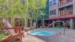 Un espace piscine comprenant un jacuzzi, un fauteuil de relaxation en bois et une terrasse en pierre.