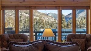 Une pièce dotée de grandes fenêtres donnant sur les montagnes, de deux fauteuils à motifs et d’une table avec une lampe.