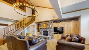 Un salon spacieux avec une cheminée en pierre, un escalier en bois, des canapés en cuir et un grand téléviseur.