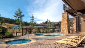 A pool area with two hot tubs, lounge chairs, and a stone pillar. - Ski in, Ski out 2 Bedroom Mountain Condo at the Base of Peak 7 with Quick Access to Historic Downtown Breckenridge (Breckenridge)