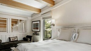 A bedroom with a large bed, a chair, a desk, and a window with a view of trees.