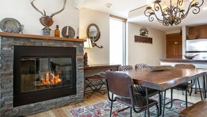 A dining area with a stone fireplace, a chandelier, and a large wooden table.