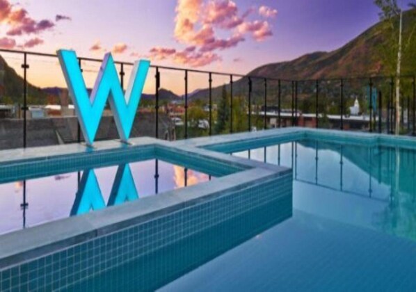 A swimming pool with a large 'W' logo, surrounded by a fence and a mountainous landscape in the background.