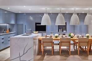 Cozinha moderna com ilha de mármore, iluminação pendente e espaço de jantar para seis pessoas.