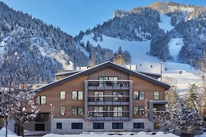 A multi-story hotel with a modern design, located in a snowy mountainous area with ski slopes visible in the background.