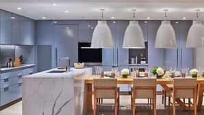 A modern kitchen with a marble island, pendant lighting, and a dining area with wooden chairs and a table set for six. - Downtown Aspen Luxury 2 Bedroom Residence (Aspen)