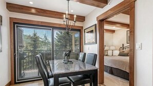 A dining area with a large table, chairs, and a chandelier. There is a sliding glass door leading to a balcony with a view of trees. - 2 Bedroom Antlers Vacation Rental With Incredible Slopeside Views and Just a Short Walk to Gondola and Lionshead Village (Vail)