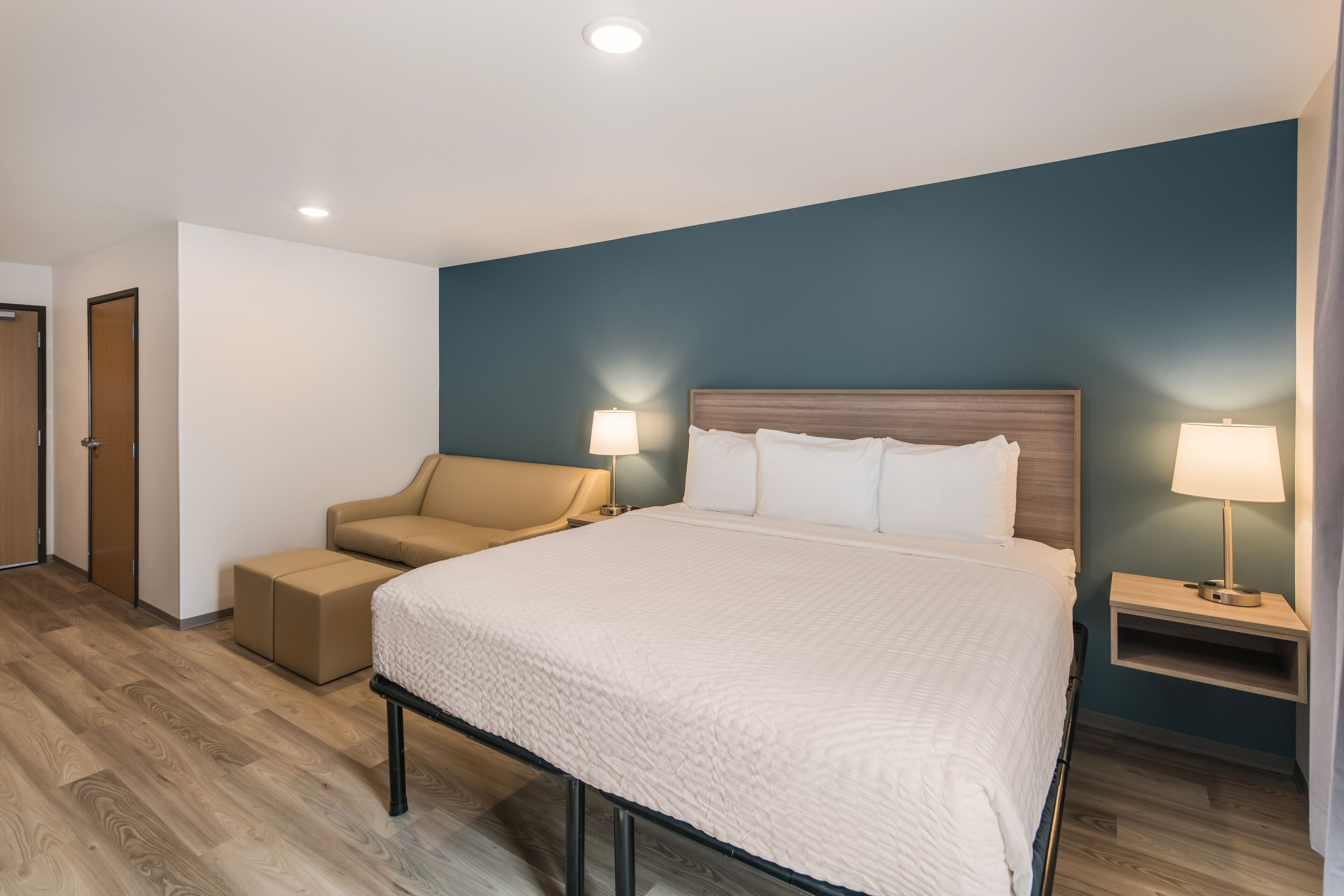 Una habitación de hotel con una cama grande, un sofá, dos mesitas de noche con lámparas y suelo de madera.