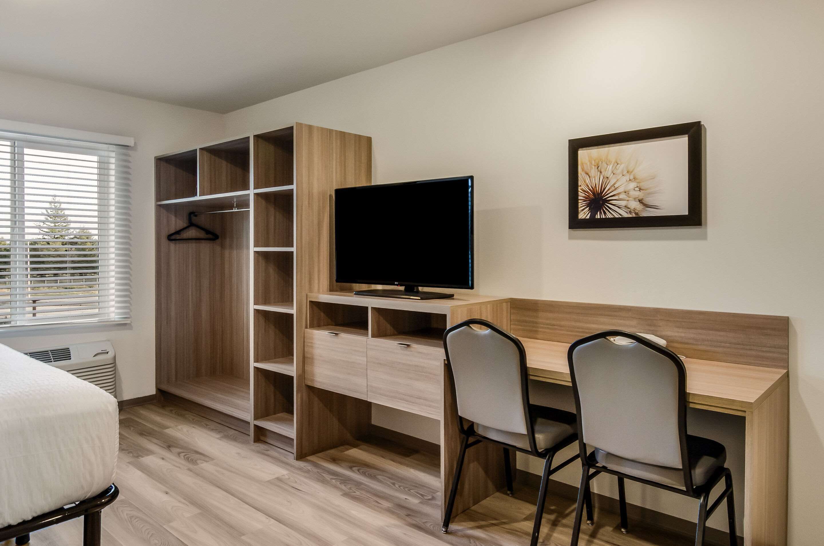 A modern bedroom with a bed, a desk with two chairs, a TV, and a wardrobe.