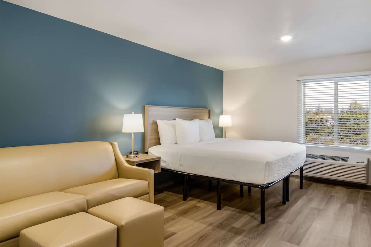 Una camera d'albergo con un letto, un divano, due lampade ai lati del letto e una finestra con tende.