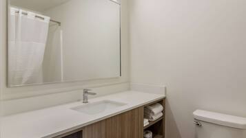 A bathroom with a white sink, a mirror, a shower curtain, and a toilet.