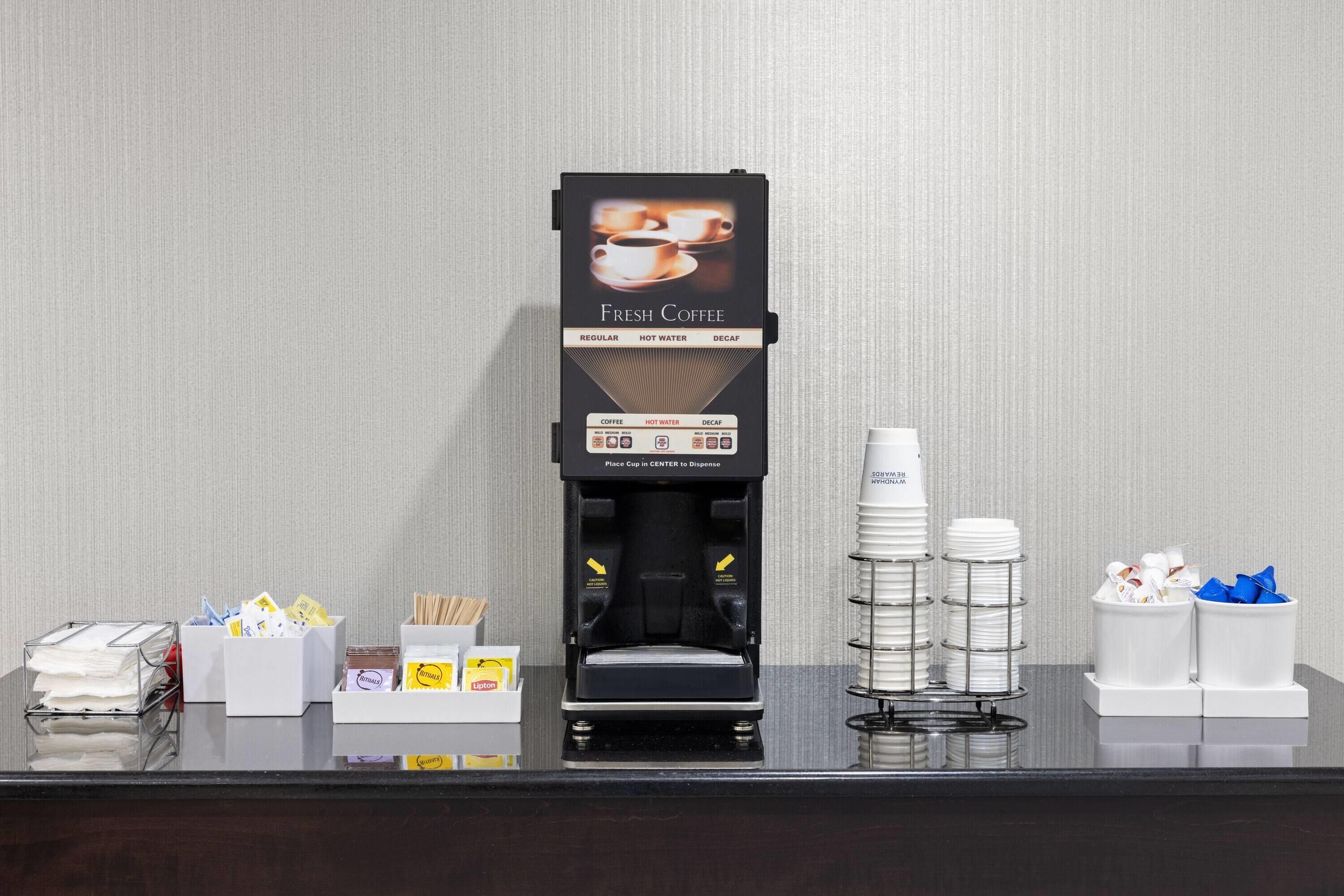 En kaffemaskine med et skilt der siger "Fresh Coffee", en stabel engangskopper og en kasse med tissuepapir.