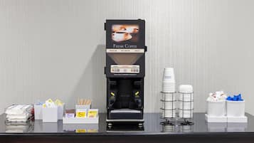 En kaffemaskine med et skilt der siger "Fresh Coffee", en stabel engangskopper og en kasse med tissuepapir.