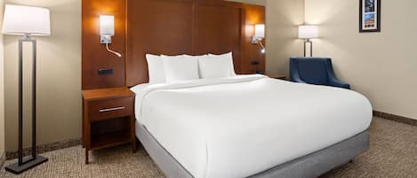 A hotel room with a large bed, two bedside tables, a chair, and wall-mounted lamps.