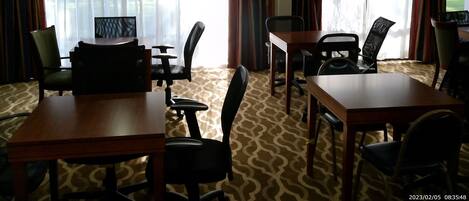 Ein Hotelzimmer mit Essbereich, inklusive Tisch und Stühlen, großen Fenstern mit Vorhängen und einem gemusterten Teppich.