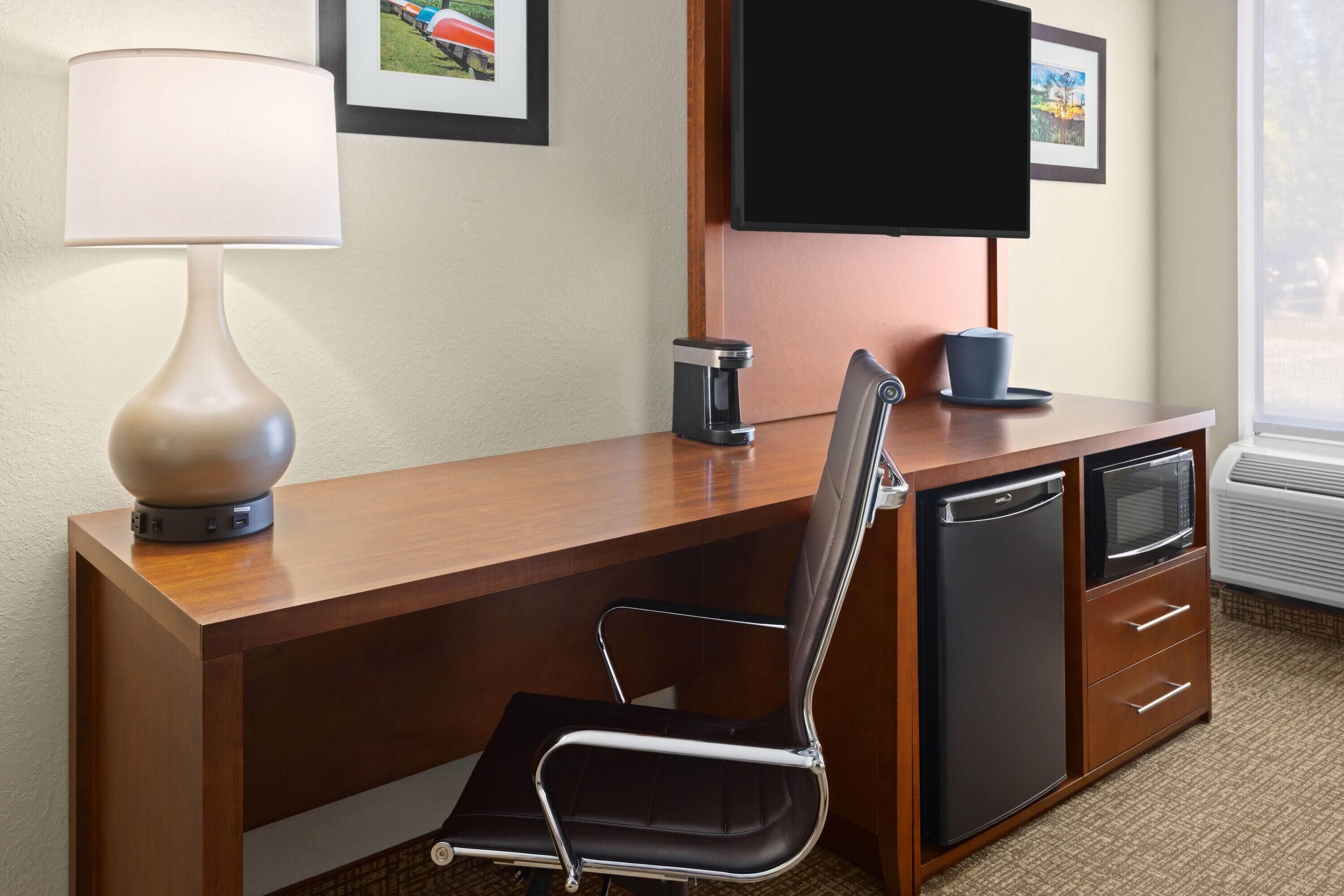 A hotel room with a wooden desk, a black office chair, a television, a coffee maker, and a microwave.