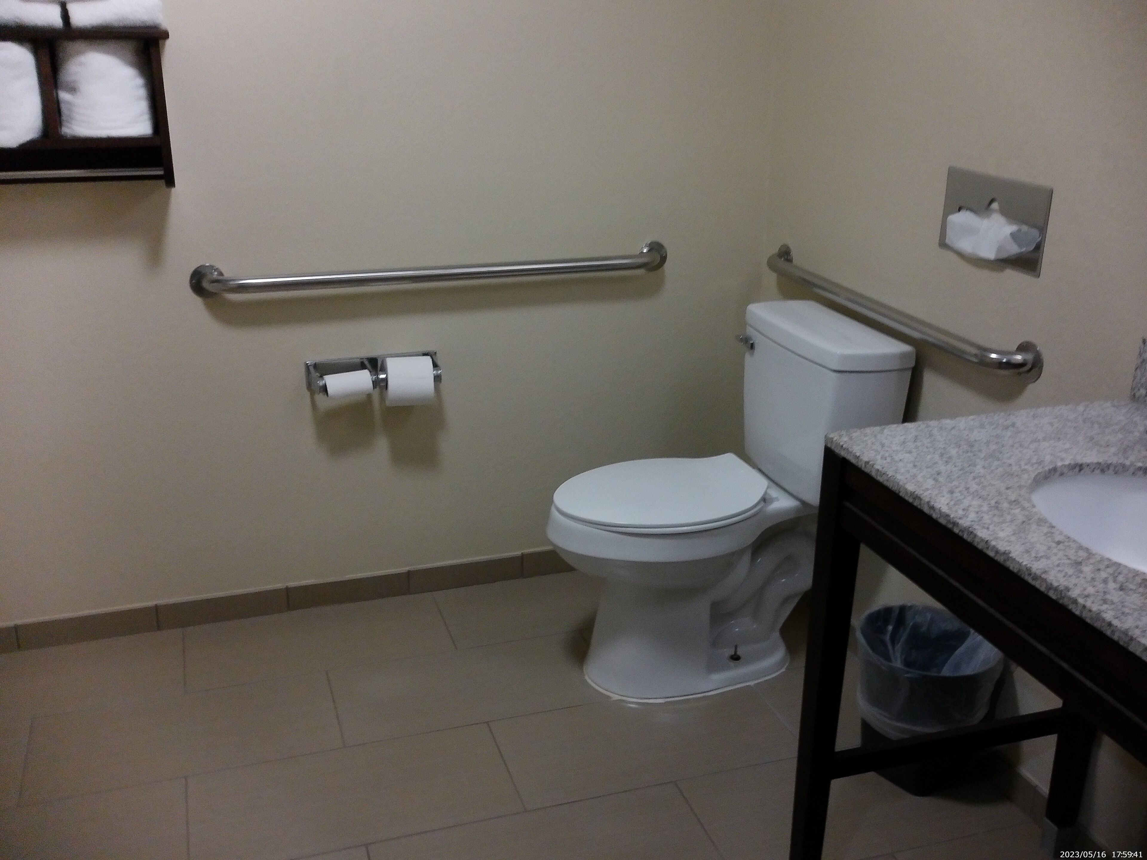 A bathroom with a toilet, a handrail, a sink, and a trash bin.