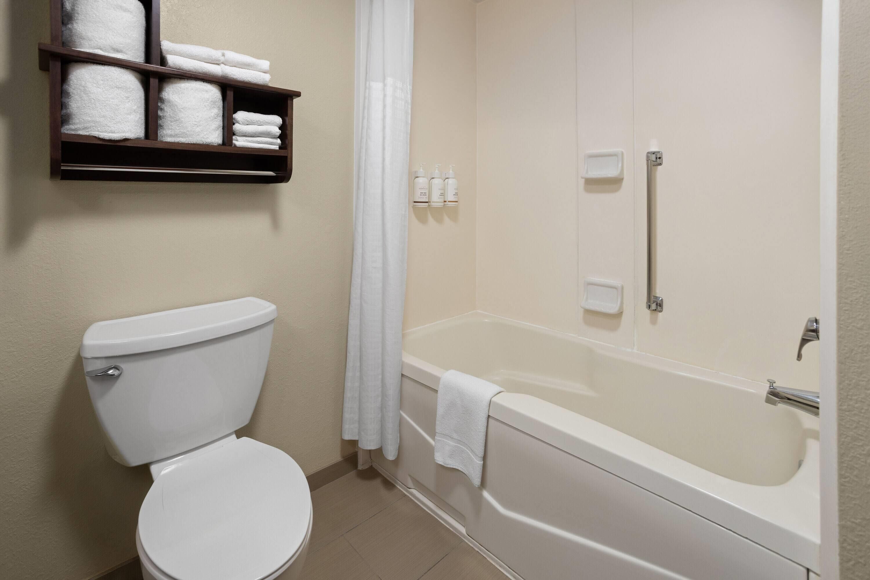 A bathroom with a toilet, a bathtub, and a shelf with towels.